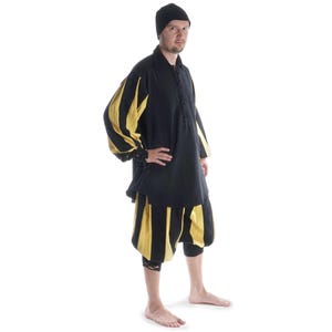Könnte beinhalten: Eine schwarze Tunika mit gelben, gestreiften Ärmeln und einer passenden gestreiften Hose. Die Tunika hat einen hohen Kragen und einen Knopfverschluss. Die Hose ist locker geschnitten und hat eine weite Beinweite.