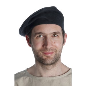 Könnte beinhalten: Ein Mann mit einer schwarzen Baskenmütze und einem hellbraunen Hemd.