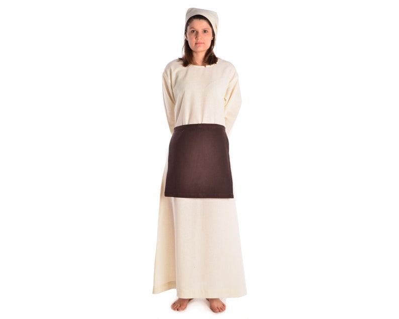 May include: A woman wearing a long, white dress with a brown apron and a white cap.