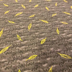 May include: A close-up of a gray textile with a pattern of yellow leaf shapes scattered across the surface. The leaves are outlined with a thin yellow line, creating a simple, yet elegant design.
