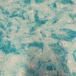 May include: A close-up of a fabric with a repeating pattern of white, stylized floral shapes against a teal and light blue background. The design has a watercolor effect, with the white lines radiating from a central point.