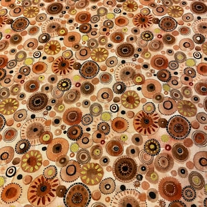 May include: A fabric with a repeating pattern of circular shapes in shades of brown, orange, and yellow. The design includes various sizes of circles, some with detailed inner patterns and black accents, set against a cream background.