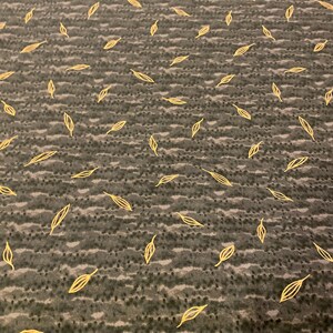 May include: Close-up of a dark gray fabric with a repeating pattern of gold-colored leaf outlines. The leaves are scattered across the surface, creating a textured and decorative design. The fabric has a subtle, wavy pattern.