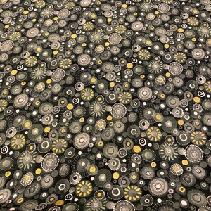 May include: Dark fabric with a repeating pattern of stylized circles in shades of gray, yellow, and white. The circles vary in size and are set against a black background, creating a textured effect.
