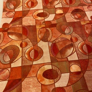 May include: Abstract geometric pattern in shades of orange, brown, and cream. The design features a repeating motif of circles, ovals, and rectangles with textured details. The overall effect is a warm, earthy, and artistic design.
