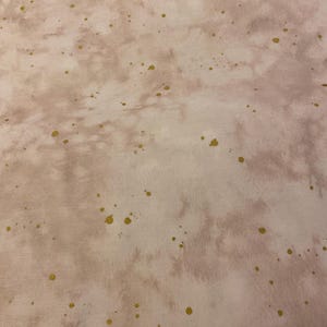 May include: A fabric with a watercolor effect in shades of pink and cream, speckled with gold metallic dots. The design has a soft, blended appearance, creating a subtle, artistic texture. Ideal for crafting or home decor projects.