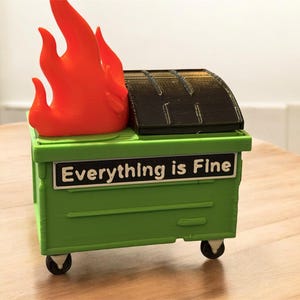 May include: A green dumpster with a black lid and orange flames on top. The dumpster has the text "Everything is Fine" on the front. The dumpster is on wheels.