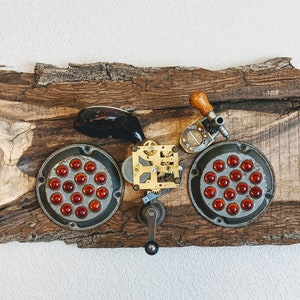 May include: A steampunk-style bicycle sculpture made from repurposed materials, including metal gears, wood, and red glass beads. The sculpture is mounted on a piece of wood with a ruler on the side.