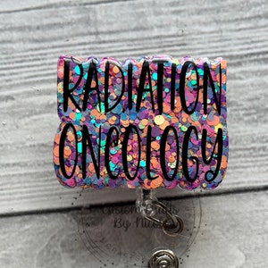 May include: A pink, blue, and purple glitter badge holder with the text "RADIATION ONCOLOGY" in black lettering.