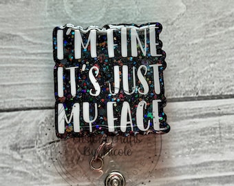 Pode incluir: Um porta-crachá preto e brilhante com o texto "I'M FINE IT'S JUST MY FACE" em branco. O porta-crachá tem um cordão retrátil de plástico transparente e um clipe de metal.