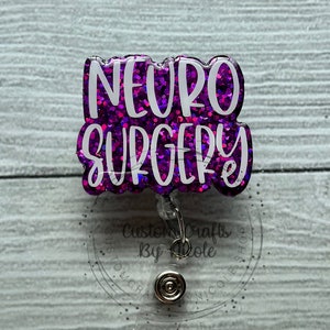 May include: Purple glitter badge reel with the text "NEURO SURGERY" in white lettering. The badge reel has a clear plastic backing and a silver retractable clip.
