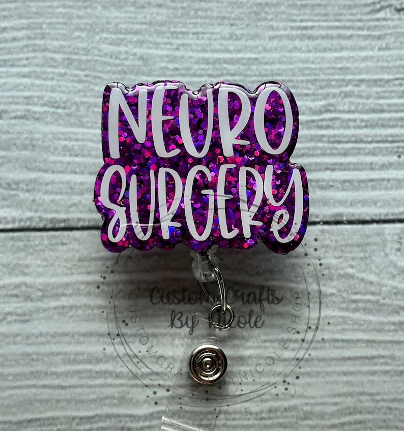 May include: Purple glitter badge reel with the text "NEURO SURGERY" in white lettering. The badge reel has a clear plastic backing and a silver retractable clip.