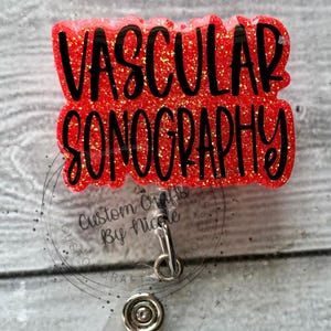 May include: Red glitter badge holder with a black text overlay that reads "Vascular Sonography". The badge holder has a clear plastic backing and a metal clip.