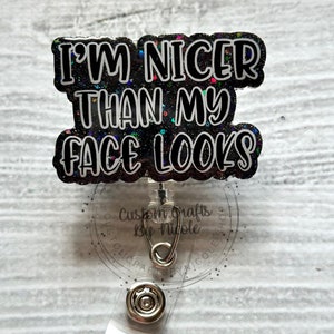 May include: A black and white glitter badge holder with the text "I'm Nicer Than My Face Looks". The badge holder has a clear plastic clip and a silver metal swivel.