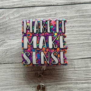 May include: A colorful glitter badge holder with the text "MAKE IT MAKE SENSE" in white letters. The badge holder is attached to a clear retractable badge reel.