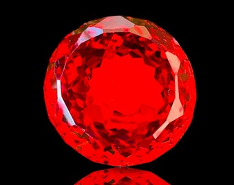 May include: A large, faceted, red gemstone with a reflective surface. The gemstone is on a black background.