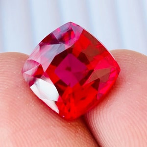 May include: A deep red, cushion-cut gemstone with a high polish.