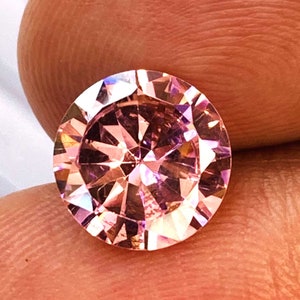 May include: A round, pink gemstone with a faceted cut. The gemstone is set in a clear, round setting.