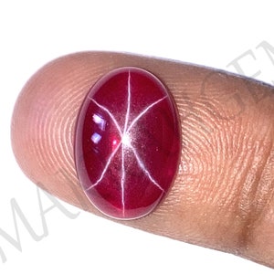 May include: A red star ruby gemstone with a starburst pattern. The ruby is oval shaped and is set in a finger ring.