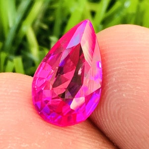 Puede incluir: Una piedra preciosa rosa en forma de pera con facetas que crean un efecto arcoíris.