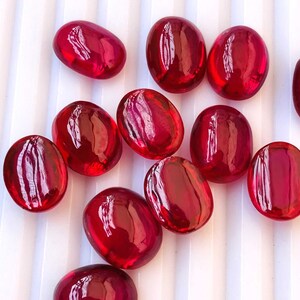 Peut inclure: Une collection de pierres précieuses rouges de forme ovale. Les pierres précieuses sont lisses et polies, avec une finition brillante.