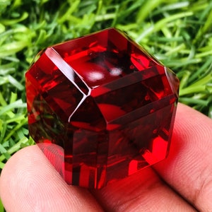 Może przedstawiać: Czerwony, fasetowany sześcian z kryształu o gładkim, polerowanym wykończeniu.