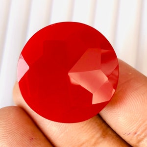 May include: A bright red round gemstone with a faceted cut.