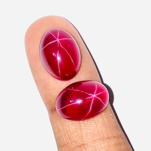 May include: Two red star ruby cabochons, one slightly larger than the other, with a star-like pattern visible in the center of each stone.