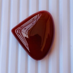 May include: A deep red, polished, heart-shaped cabochon gemstone.