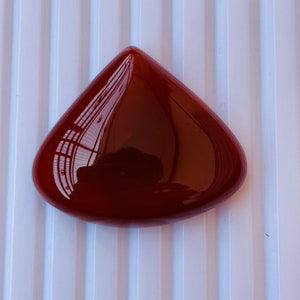 May include: A deep red, teardrop-shaped cabochon gemstone with a smooth, polished surface.