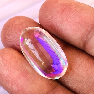 Könnte beinhalten: Ein klarer, irisierender Edelstein mit einem Regenbogen-Schimmer. Der Edelstein ist oval geformt und hat eine glatte, polierte Oberfläche.