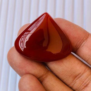 May include: A teardrop-shaped, polished carnelian gemstone with a deep red colour.