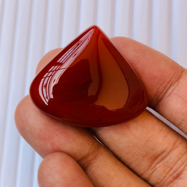 May include: A teardrop-shaped, polished carnelian gemstone with a deep red colour.