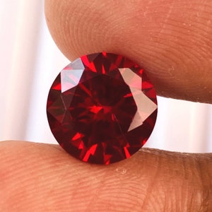 May include: A deep red round gemstone with many facets.
