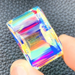 May include: A clear, faceted crystal with rainbow iridescent colors. The crystal is shaped like a rectangle with rounded corners.