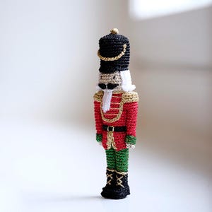 May include: A crocheted nutcracker doll with a black hat, red and green uniform, and a white beard.