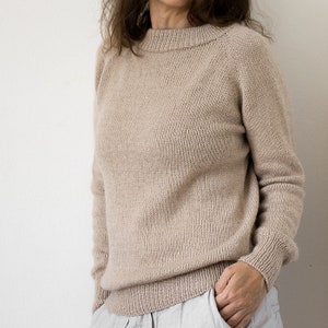 May include: A beige knitted jumper with a round neckline and long sleeves.