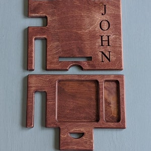 May include: A two-piece wooden organizer with a phone stand and a tray with compartments. The organizer is stained a dark brown color and has the name "JOHN" engraved on the side.