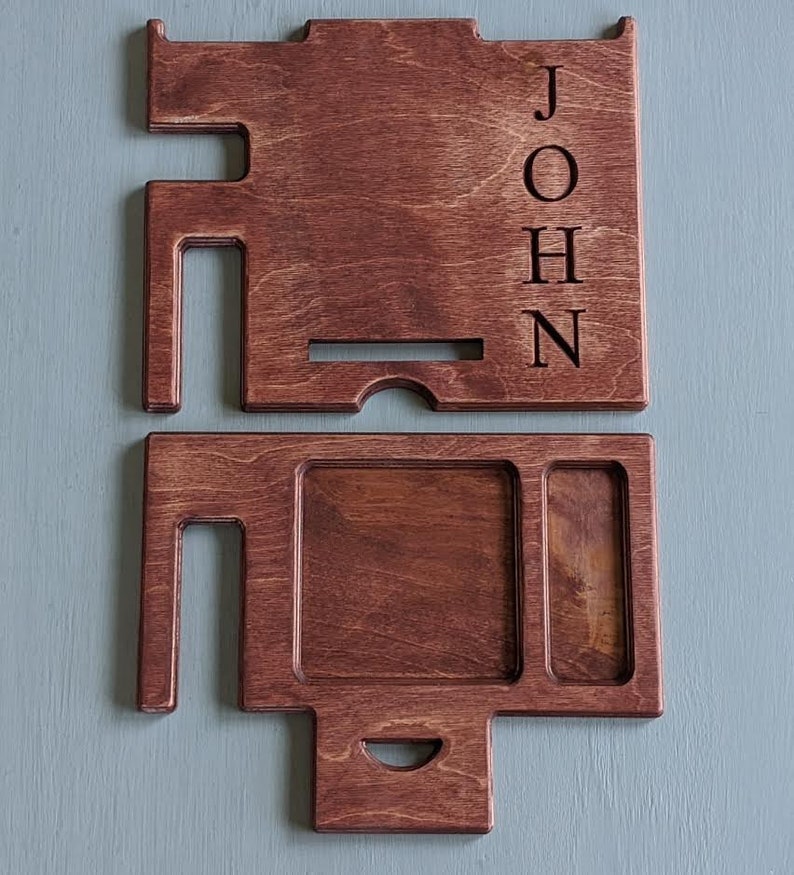 May include: A two-piece wooden organizer with a phone stand and a tray with compartments. The organizer is stained a dark brown color and has the name "JOHN" engraved on the side.