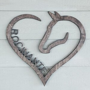 May include: A wooden heart-shaped sign with a horse head silhouette and the word "ROCI NANTE" carved into it.