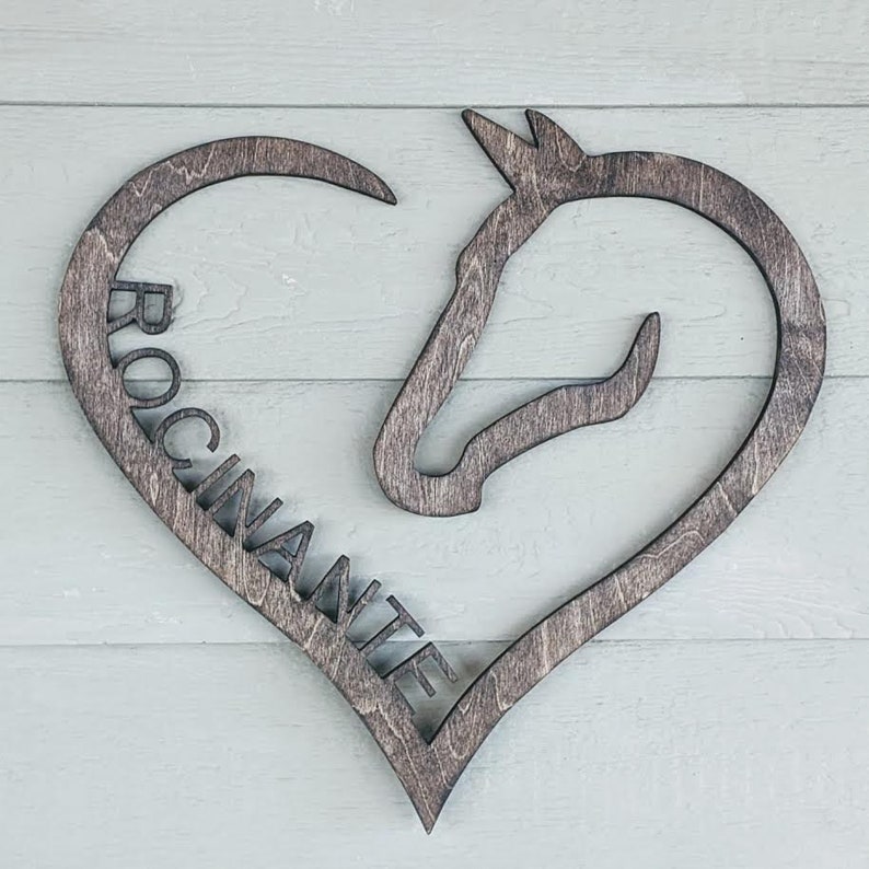 May include: A wooden heart-shaped sign with a horse head silhouette and the word "ROCI NANTE" carved into it.