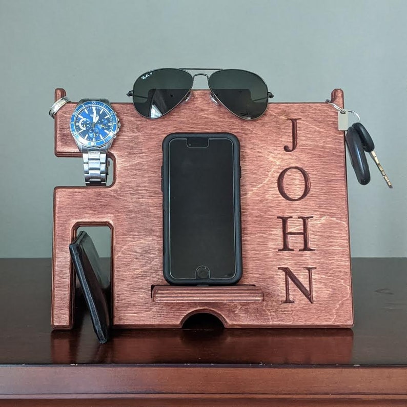 May include: A wooden stand with a phone holder, watch holder, and key hook. The stand is personalized with the name "JOHN".