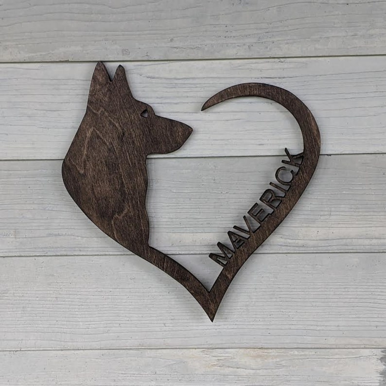 May include: A wooden heart-shaped sign with a silhouette of a German Shepherd dog's head and the name "Maverick" carved into the heart.