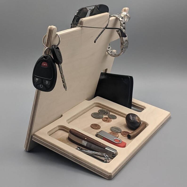 May include: A wooden organizer with slots for keys, a watch, sunglasses, a wallet, and a phone. There are also compartments for small items like coins and a pen.