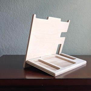 May include: A wooden stand with three compartments, designed to hold small items like phones, watches, or jewelry. The stand is made of light-colored wood and has a simple, modern design.