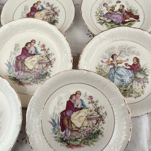 Peut inclure: Ensemble de huit assiettes en céramique blanche avec une bordure dorée. Chaque assiette présente une scène romantique différente avec des couples dans un jardin.