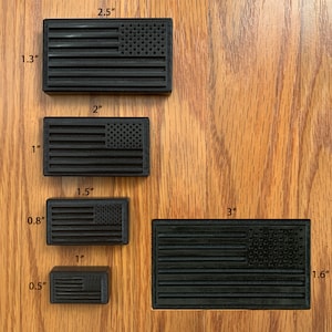 May include: Five black rectangular American flag emblems of varying sizes. The dimensions are labeled as 2.5 by 1.3 inches, 2 by 1 inch, 1.5 by 0.8 inches, 1 by 0.5 inches, and 3 by 1.6 inches. Each emblem features raised stripes and stars.