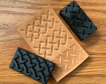 May include: Two black rubber stamps with a diamond pattern, one on top of a piece of brown leather with the same pattern embossed into it.
