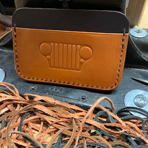 May include: A brown leather wallet with a black leather flap and a Jeep grille embossed on the front.