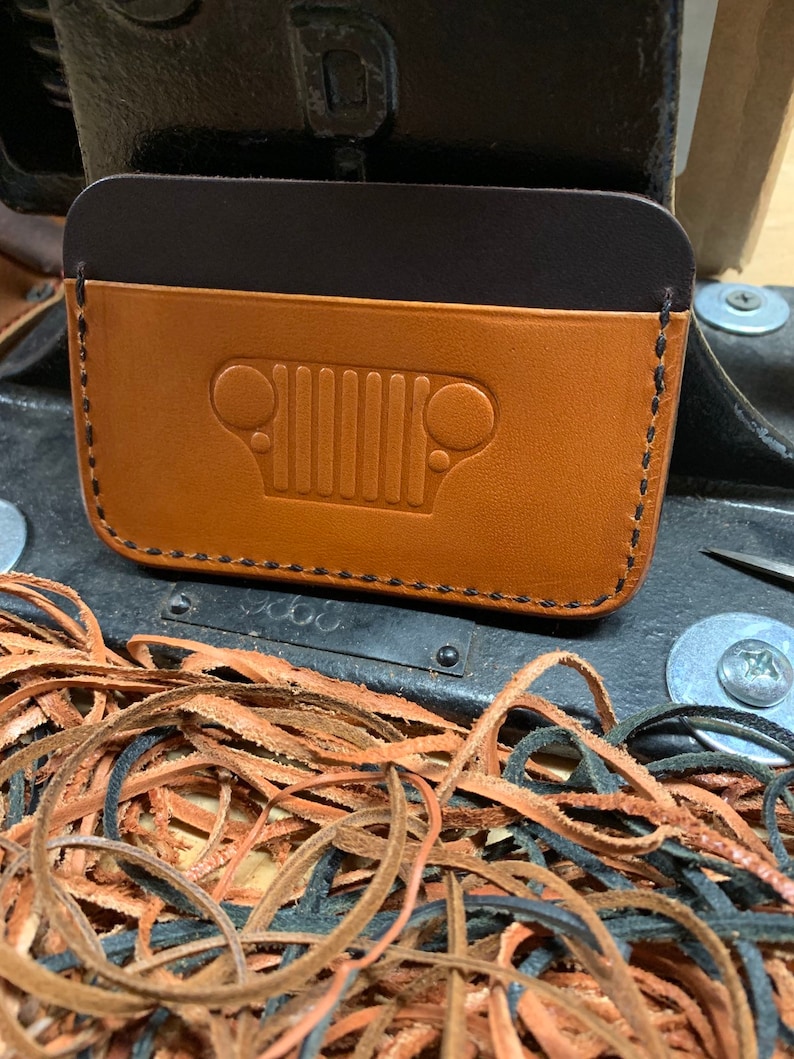 May include: A brown leather wallet with a black leather flap and a Jeep grille embossed on the front.